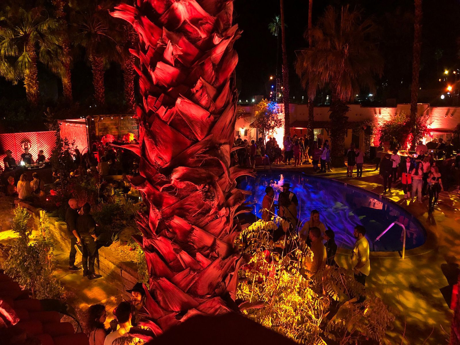 Nighttime outdoor party with a pool, red and yellow lights, and people.