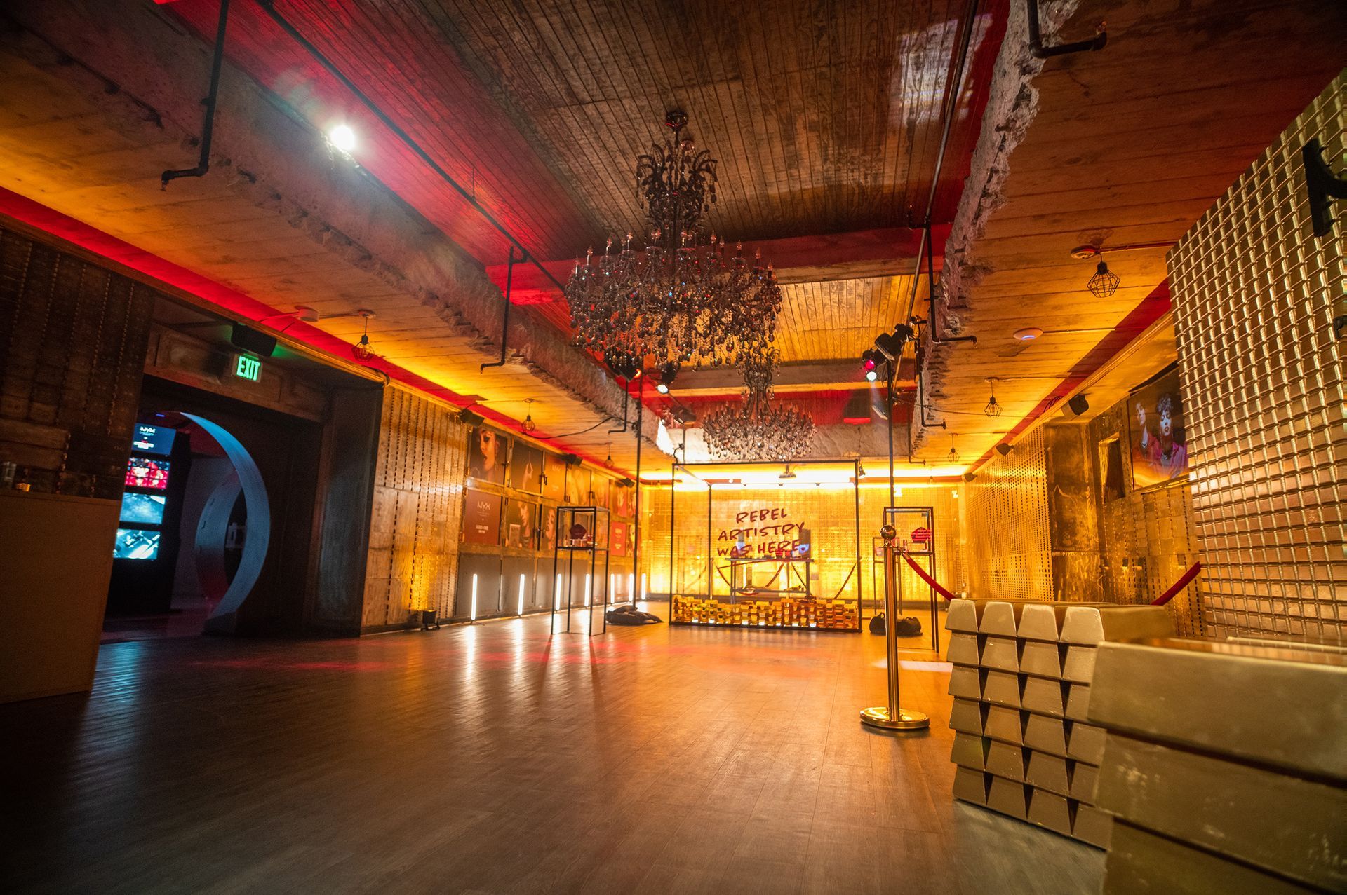 A lavish, gold-toned event space with a chandelier, large gold bar stacks, and artwork on the walls.