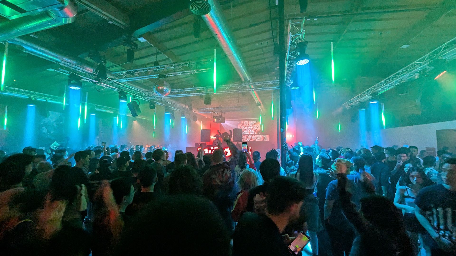 A large, crowded rave with people dancing under green and blue lights.