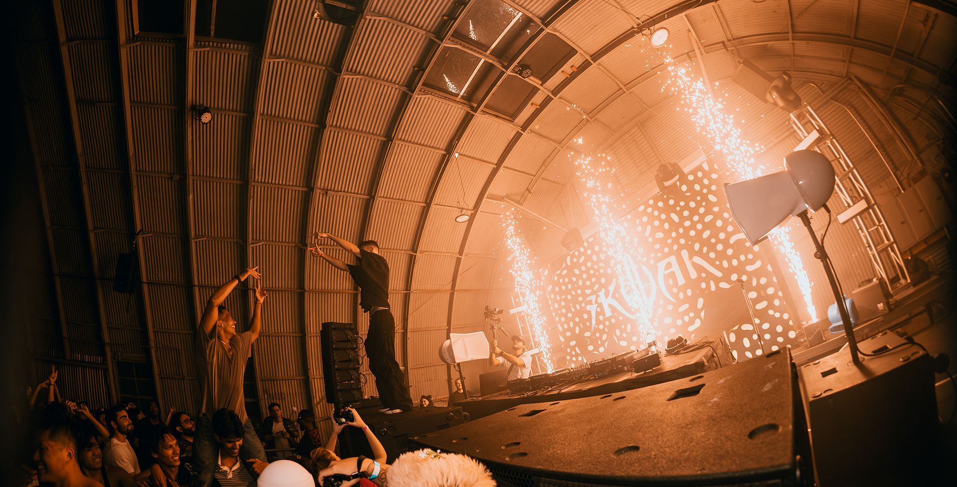 A concert stage with fireworks. A performer dances in front of the crowd, and sparks erupt.