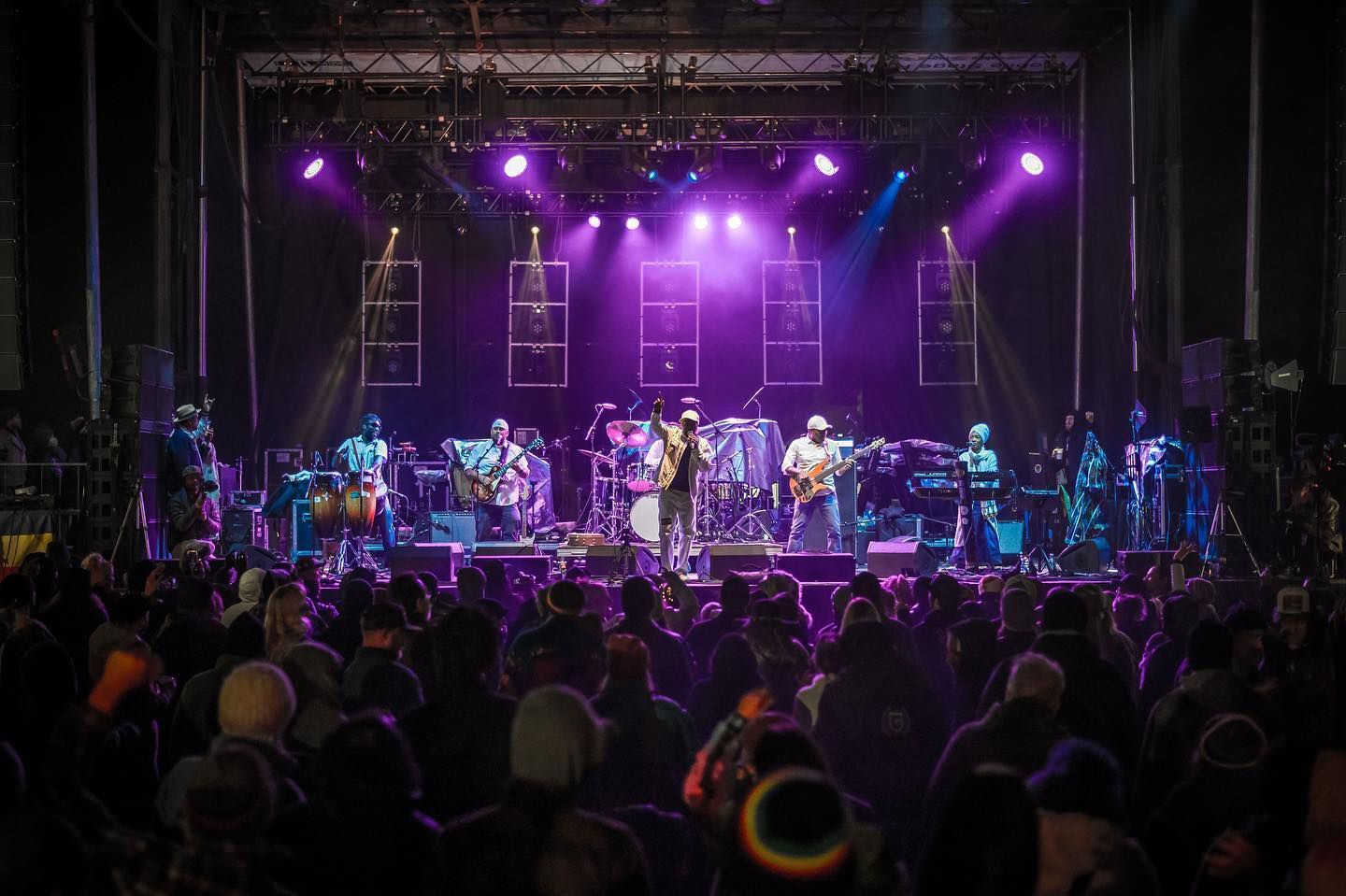 Band performing on stage under purple lights, with a crowd of people in the foreground.