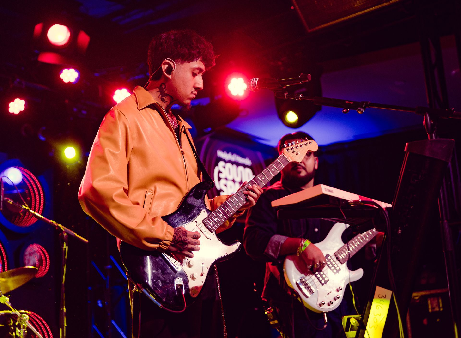 Two musicians on stage playing guitars under red and blue stage lights.