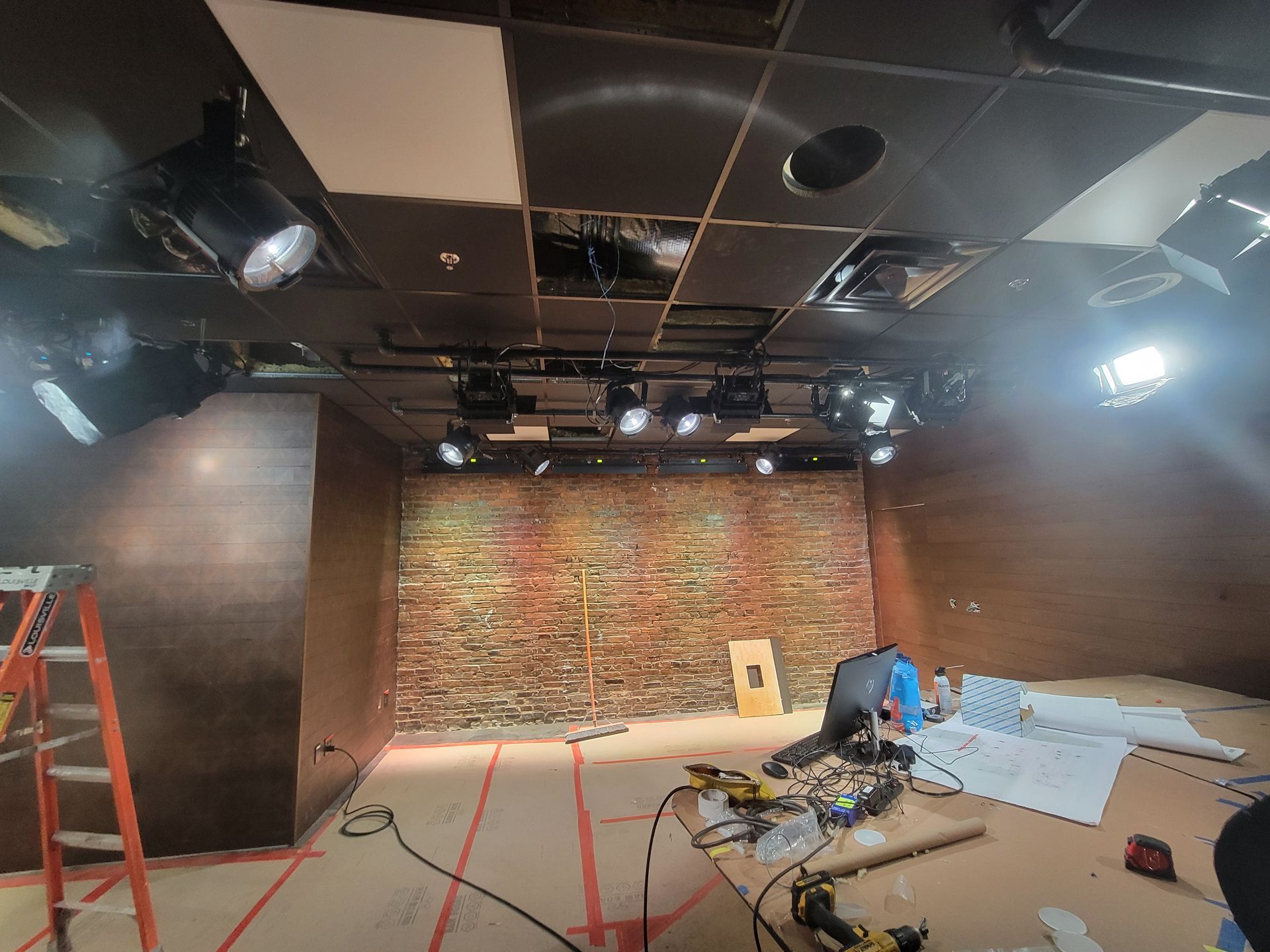 Interior shot of a studio under construction with exposed brick wall, lighting fixtures, and tools on the floor.