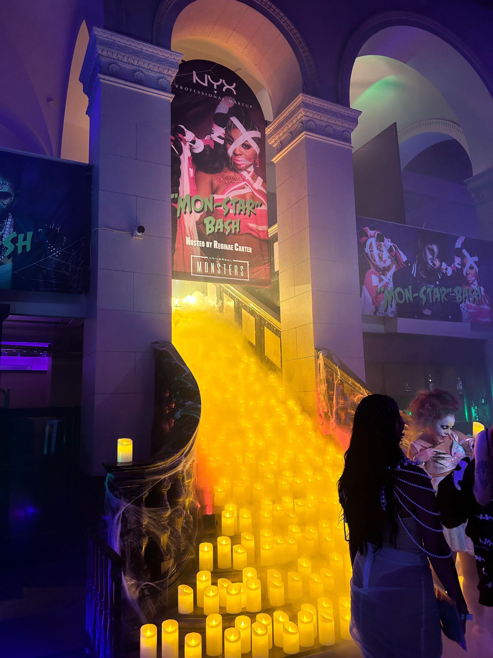 Staircase with glowing candles, decorated for an event. People in the foreground, promotional banners visible.