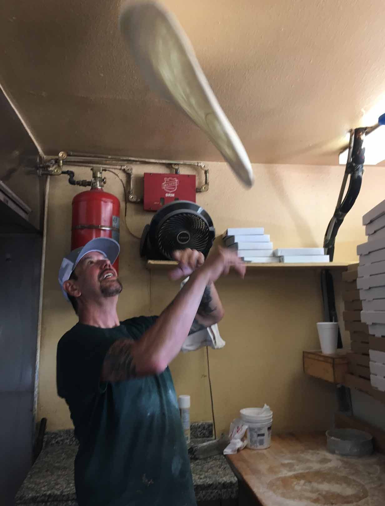 A man is throwing a pizza in the air in a kitchen