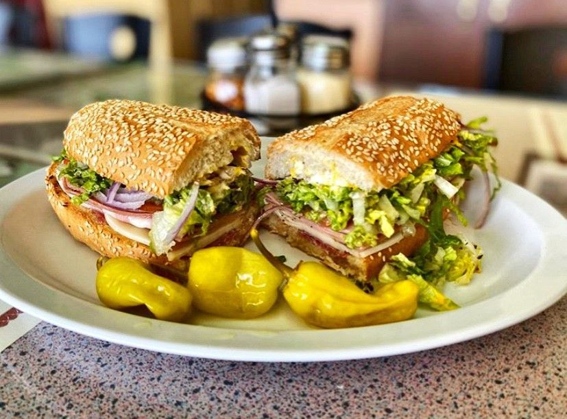 Two sub sandwiches are on a white plate with pickles.
