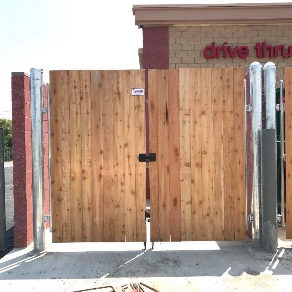 Wooden double gate blocking a drive-thru entrance beside a brick building.