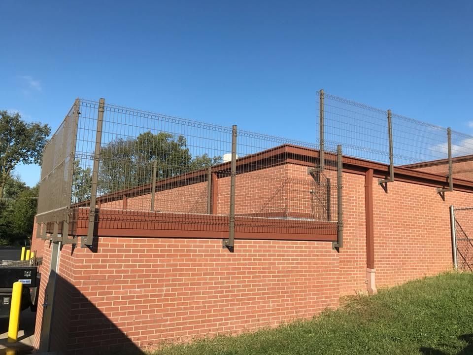 Brick building with a fenced rooftop and grassy slope under a clear blue sky