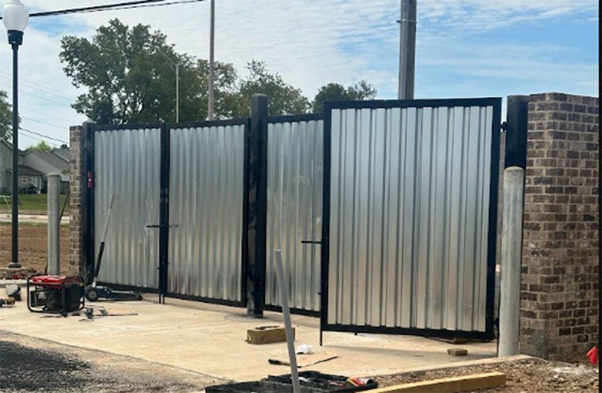Corrugated metal fence gate under construction beside a brick pillar, with tools on a concrete slab.