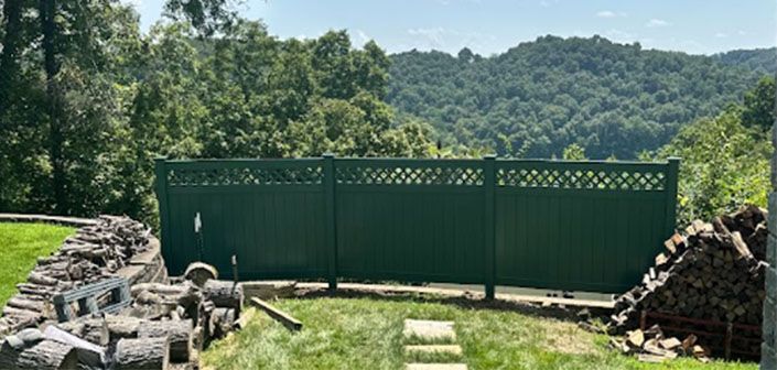 Green gate between stone walls overlooking a grassy landscape and forested hills