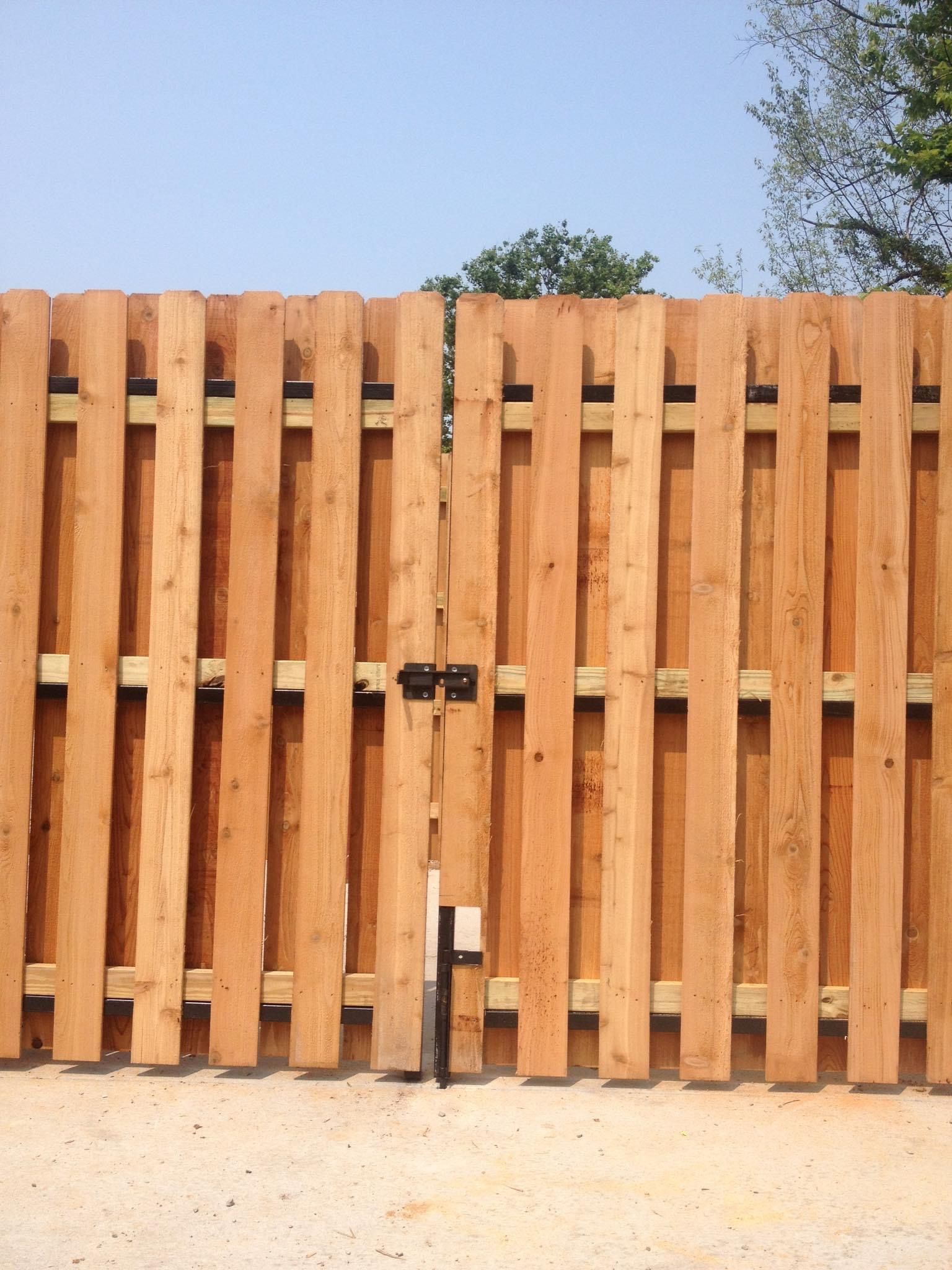 Wooden slat fence with a black latch and white post against a blue sky