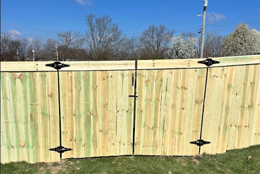Wooden backyard fence with black hinges and a central latch under a blue sky