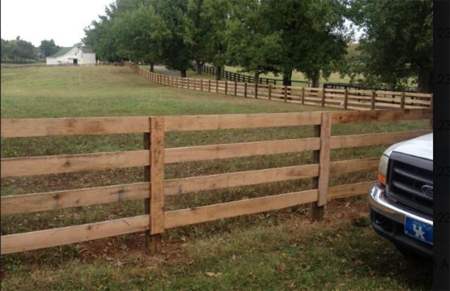 Wooden ranch fence beside a grassy field, with a truck at the right edge.
