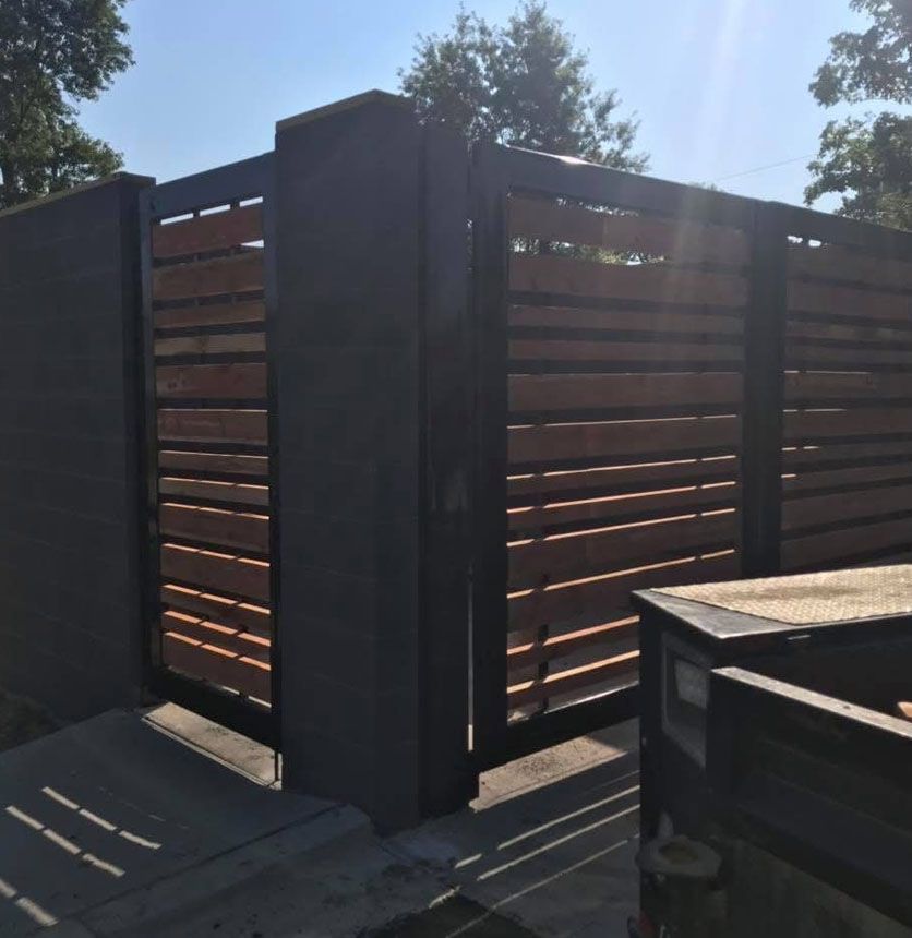 Wooden privacy fence with dark posts in bright sunlight, casting shadows on a patio.
