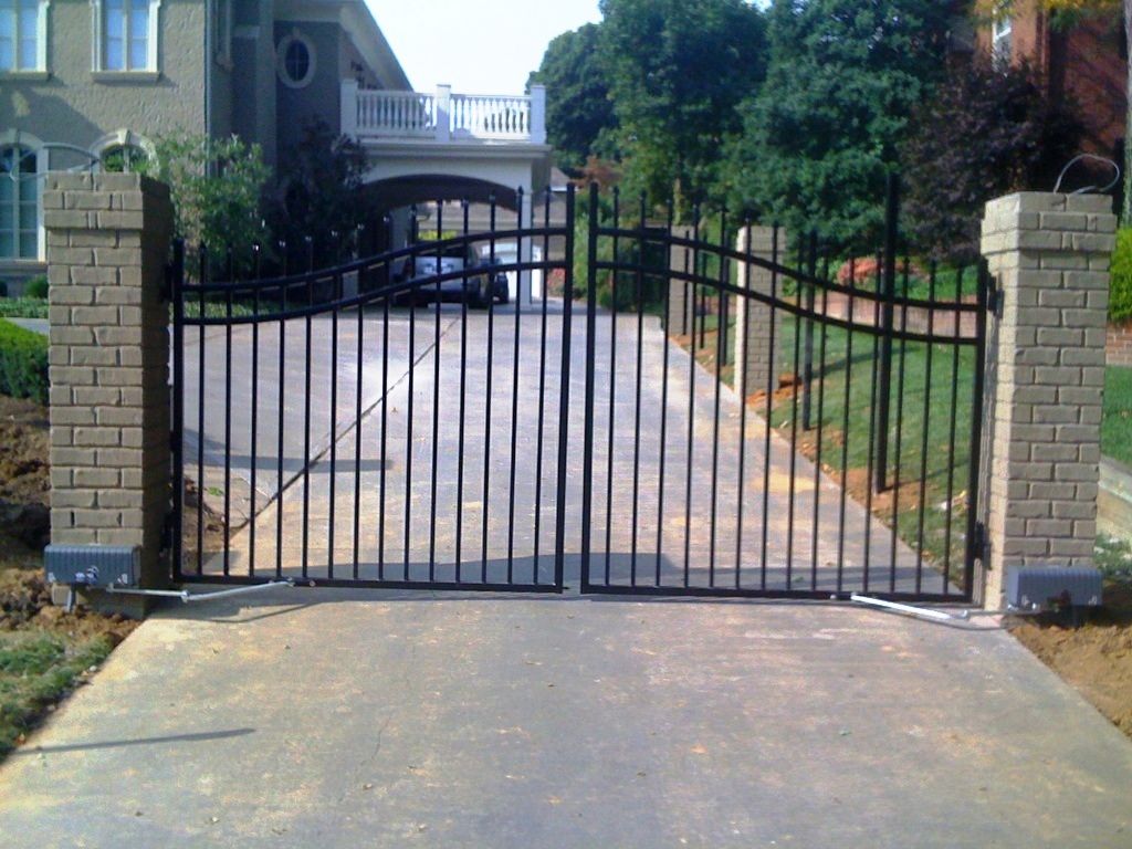 A black gate is open to a driveway in front of a house.