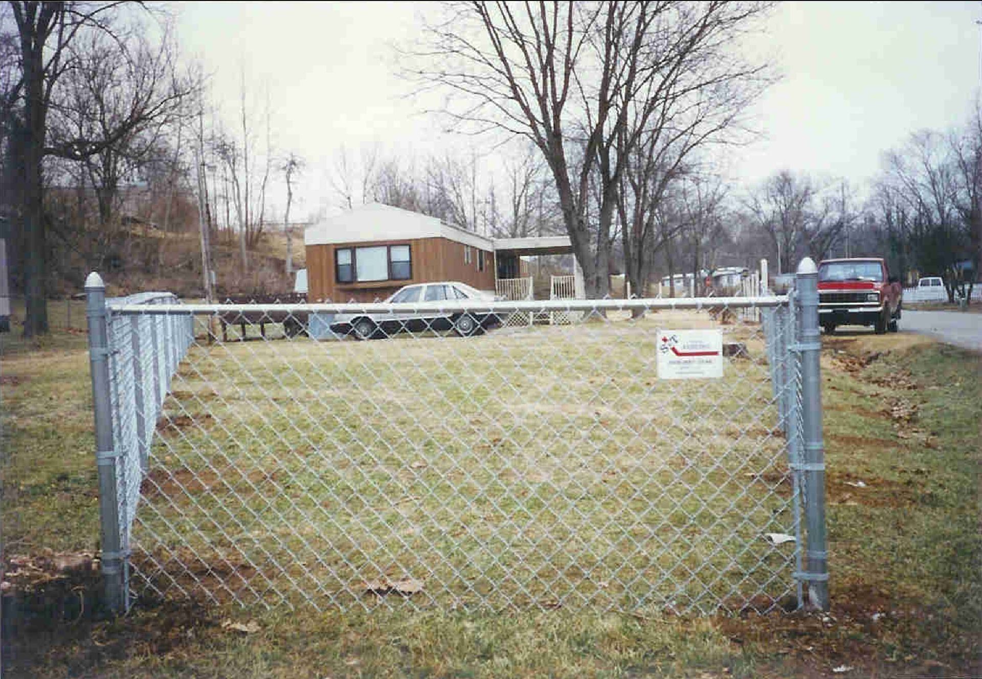 A chain link fence surrounds a yard with a house in the background.
