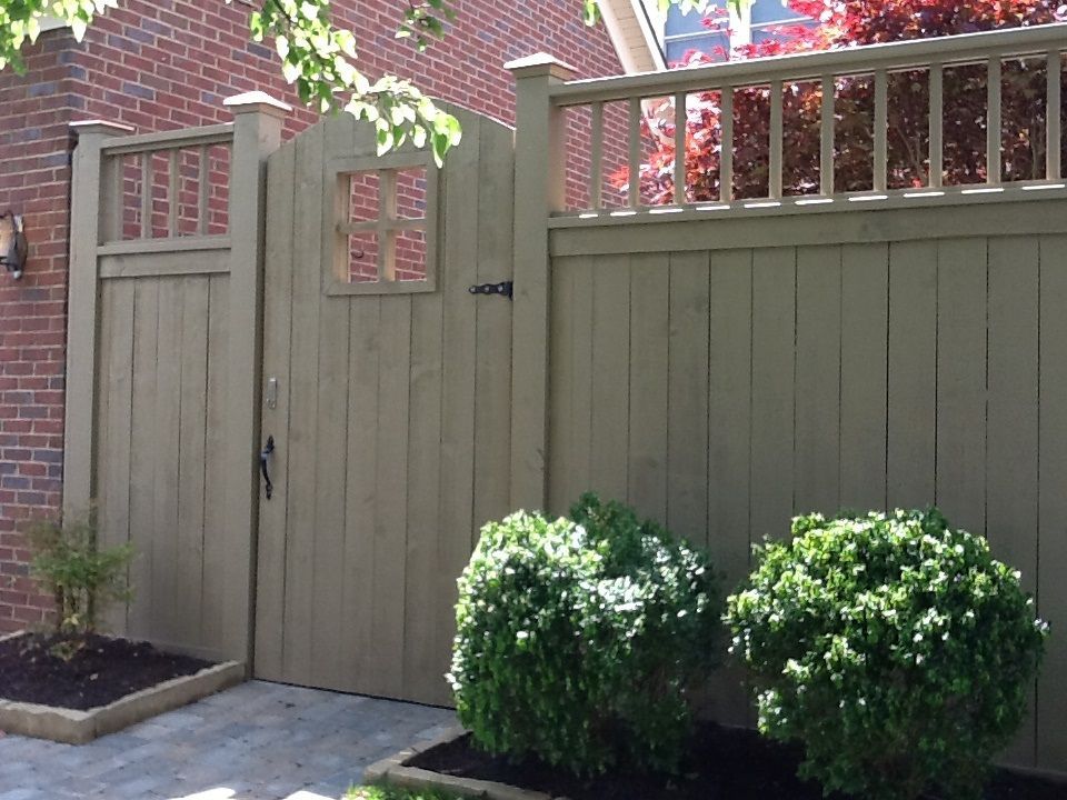 A wooden fence with a gate and bushes in front of it.