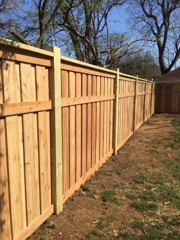 A wooden fence in a backyard with trees in the background.