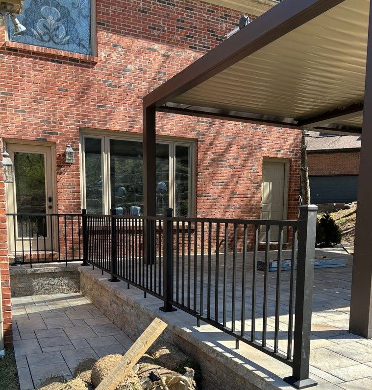 A brick house with a covered patio with a metal railing.
