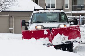 A truck with a snow plow removing snow from a driveway