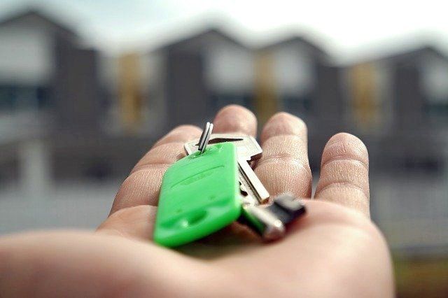 A person is holding a bunch of keys in their hand in front of a house.