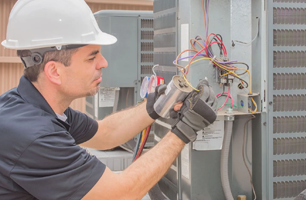 A man wearing a hard hat and gloves is working on an air conditioner.