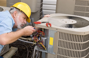 A man wearing a hard hat is working on an air conditioner.