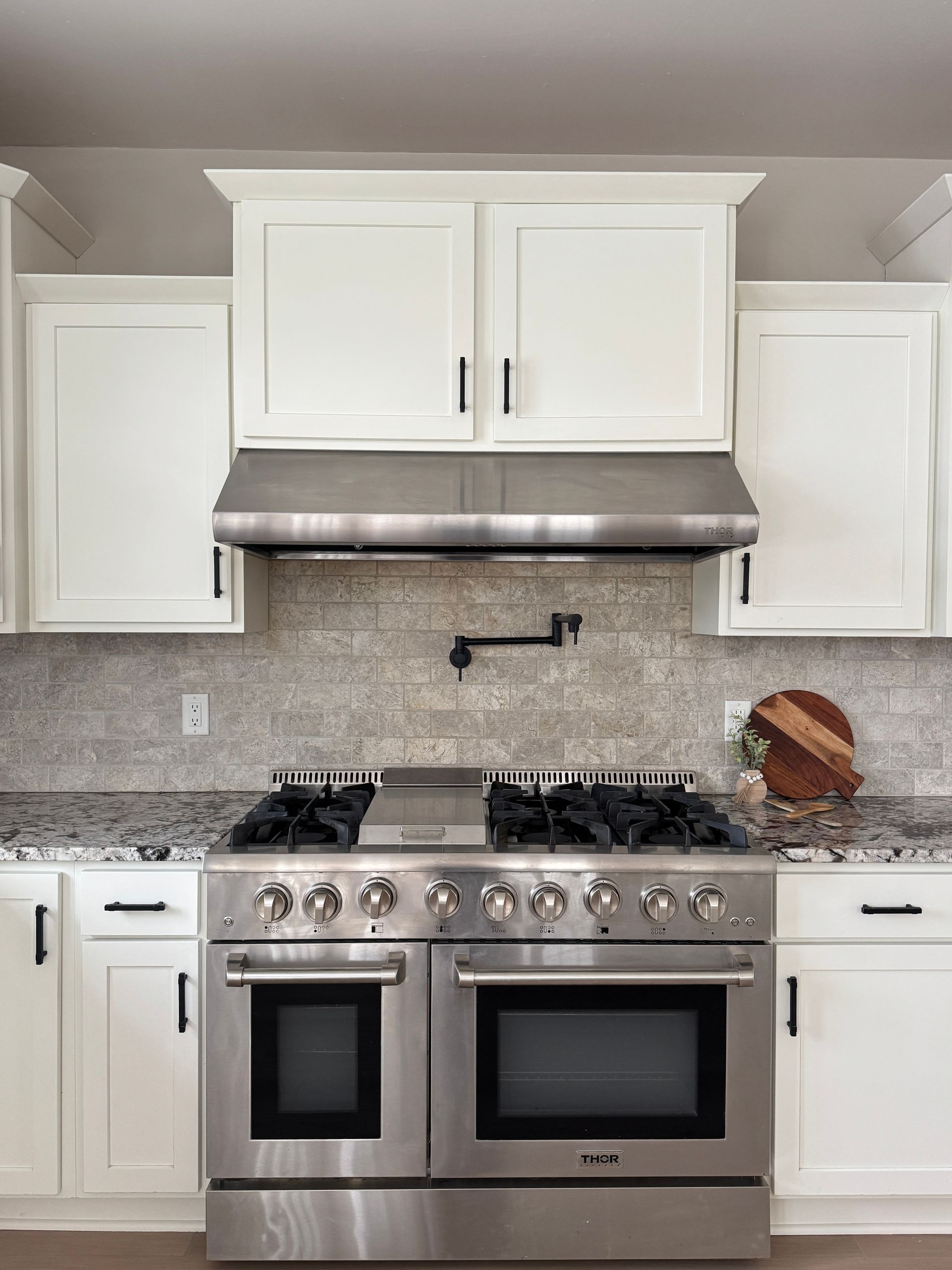 White kitchen with stainless steel oven range, cabinets, and backsplash.