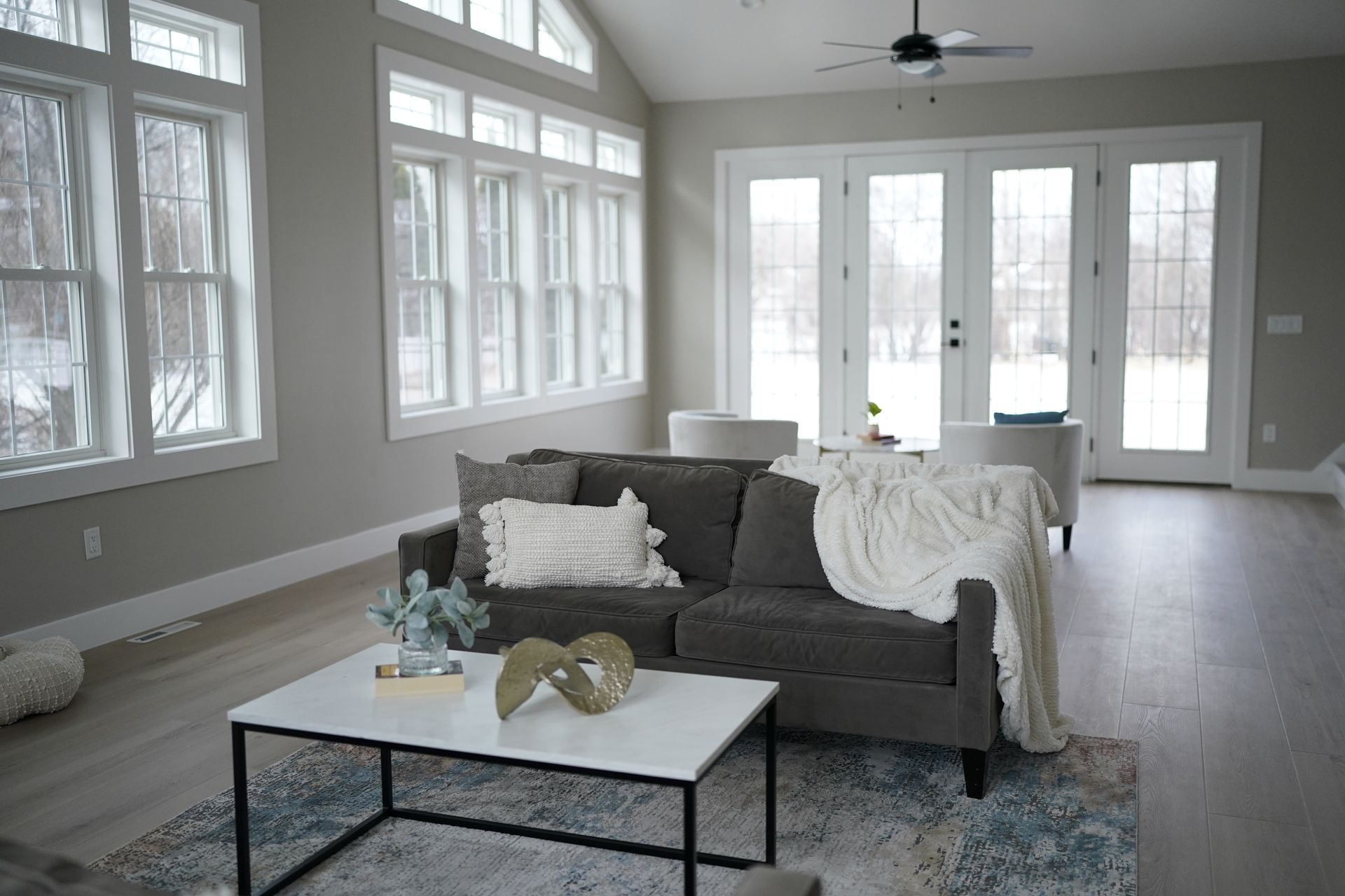 Living room with grey sofa, white coffee table, large windows, and doors overlooking a snowy landscape.