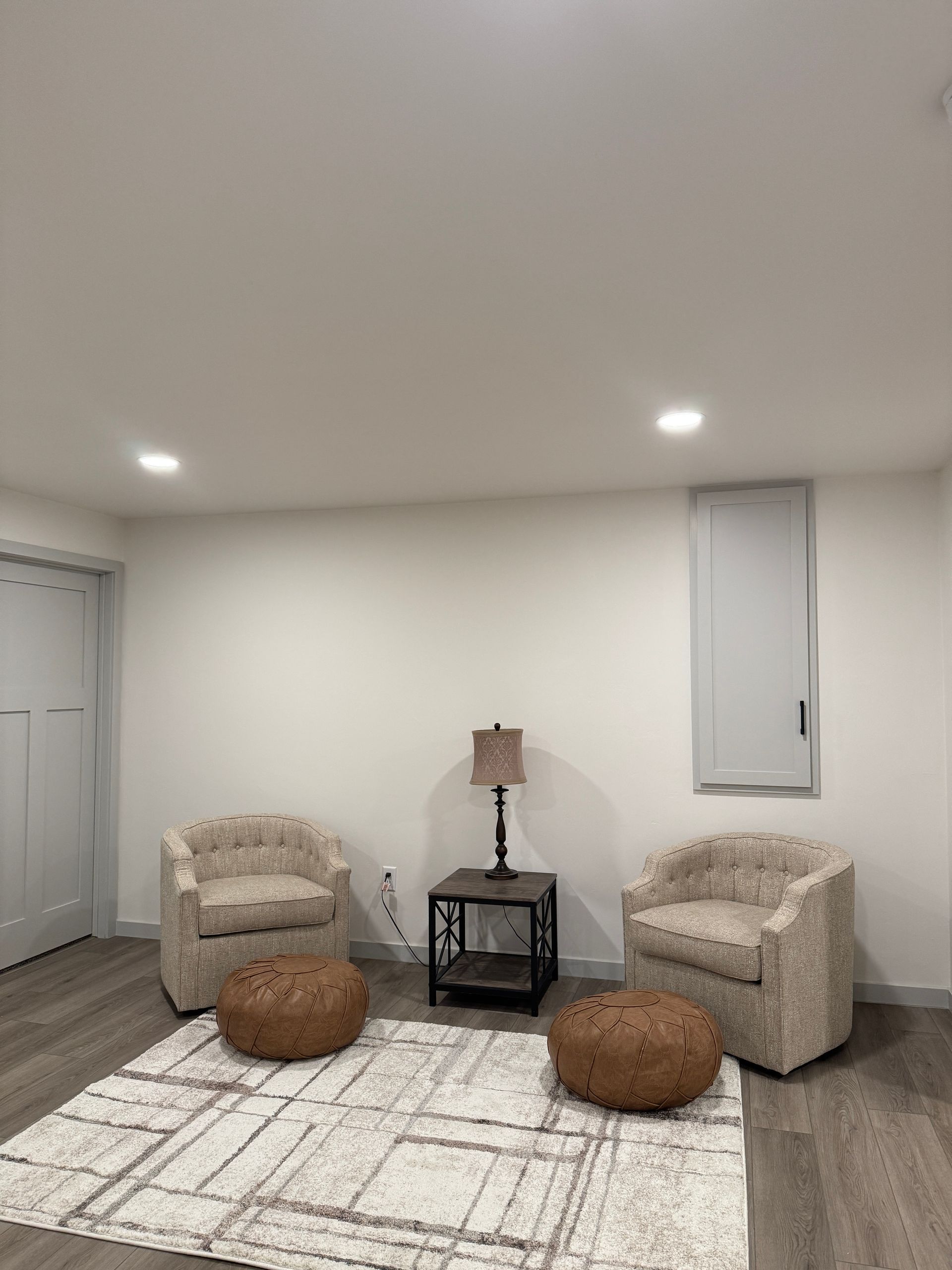 Two patterned armchairs and ottoman face each other over a rug. A side table with a lamp is between the chairs.