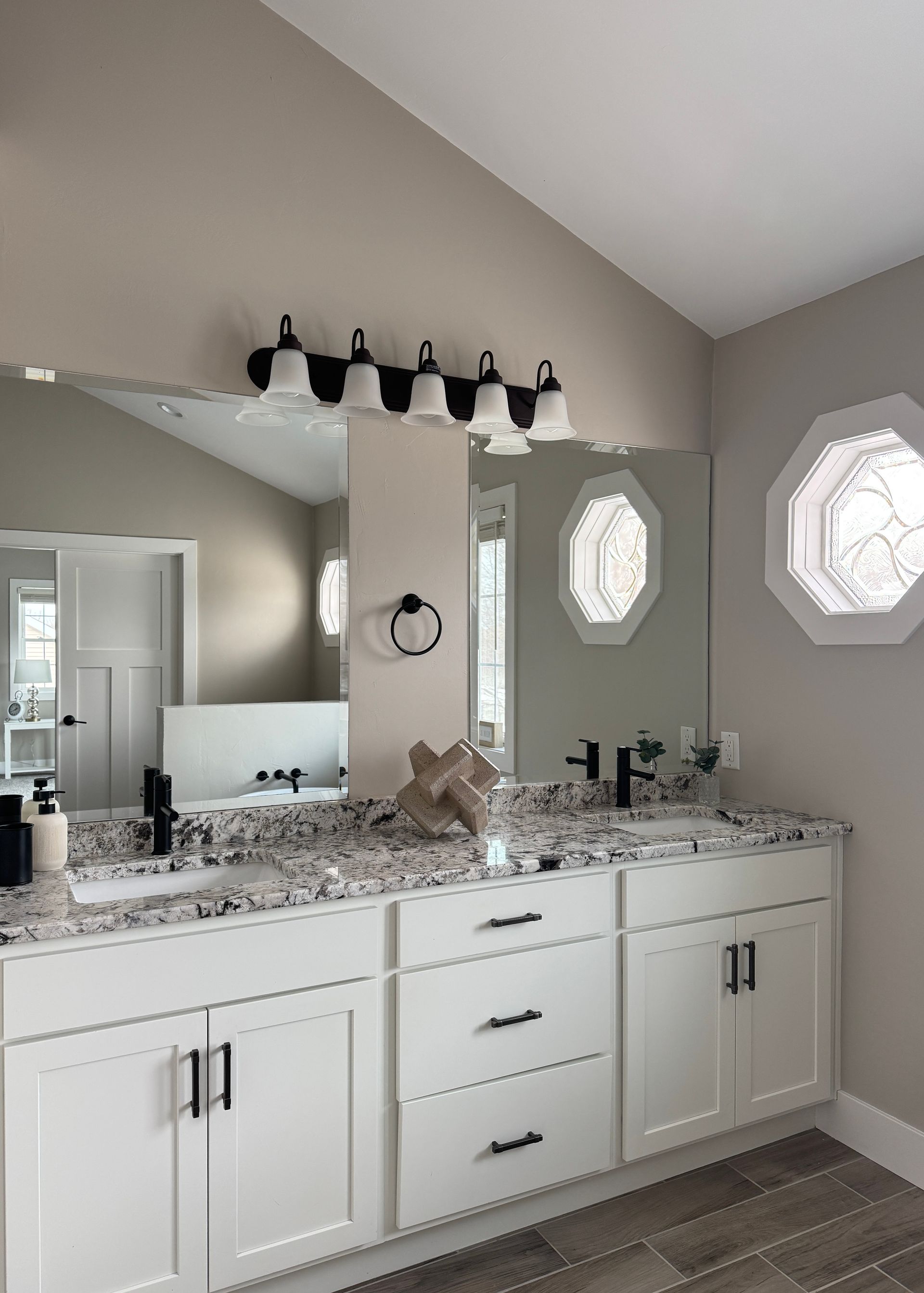 Bathroom with white vanity, speckled countertop, large mirror, black fixtures, and decorative lights.