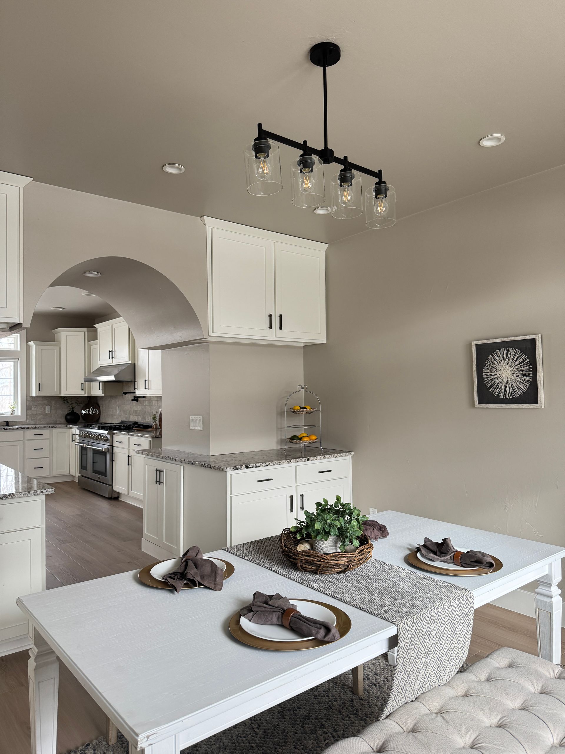 A bright kitchen and dining area with white cabinets, a dining table set for two, and a black light fixture.