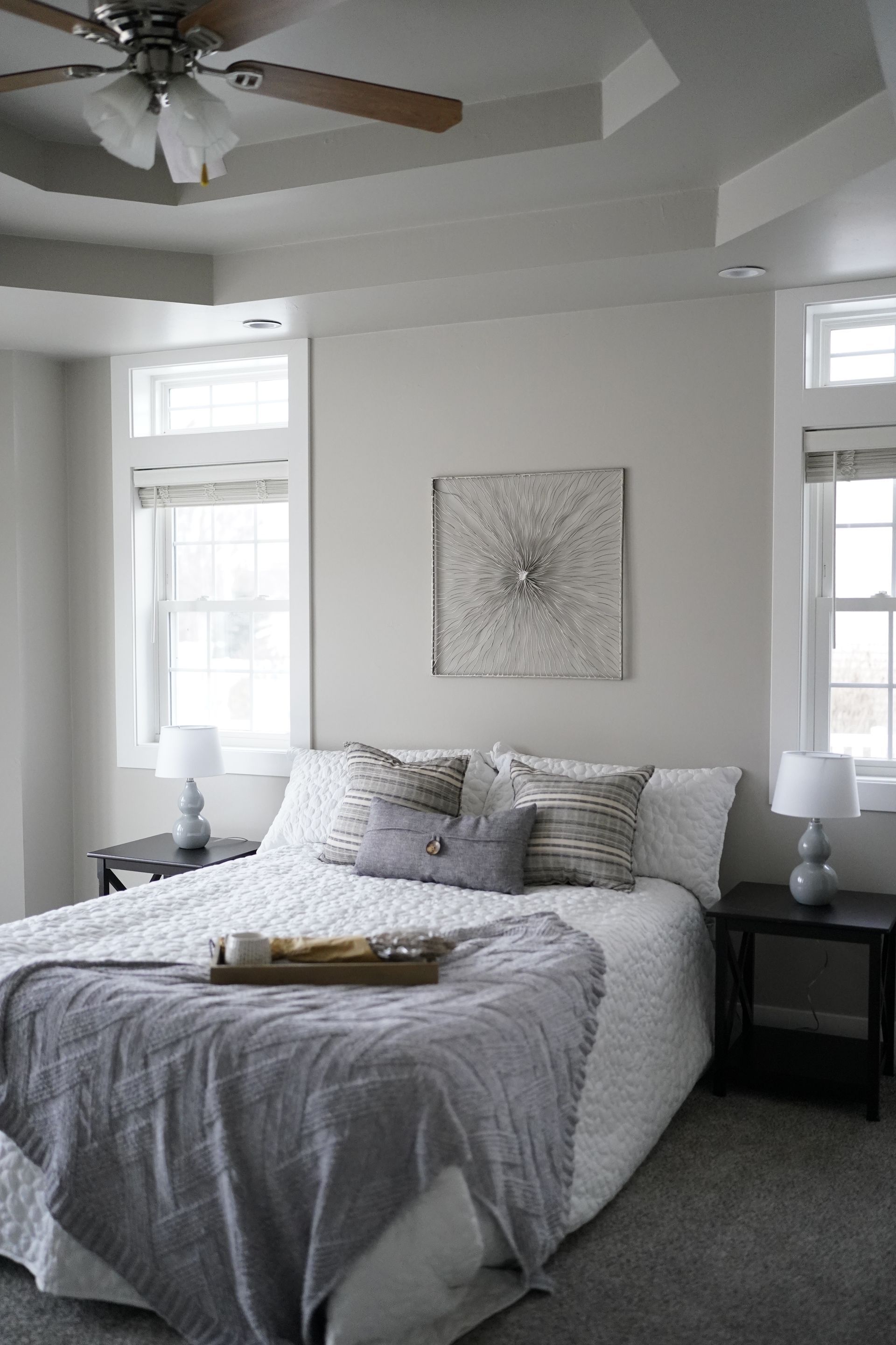 Bedroom with bed, windows, artwork, and ceiling fan in shades of gray.