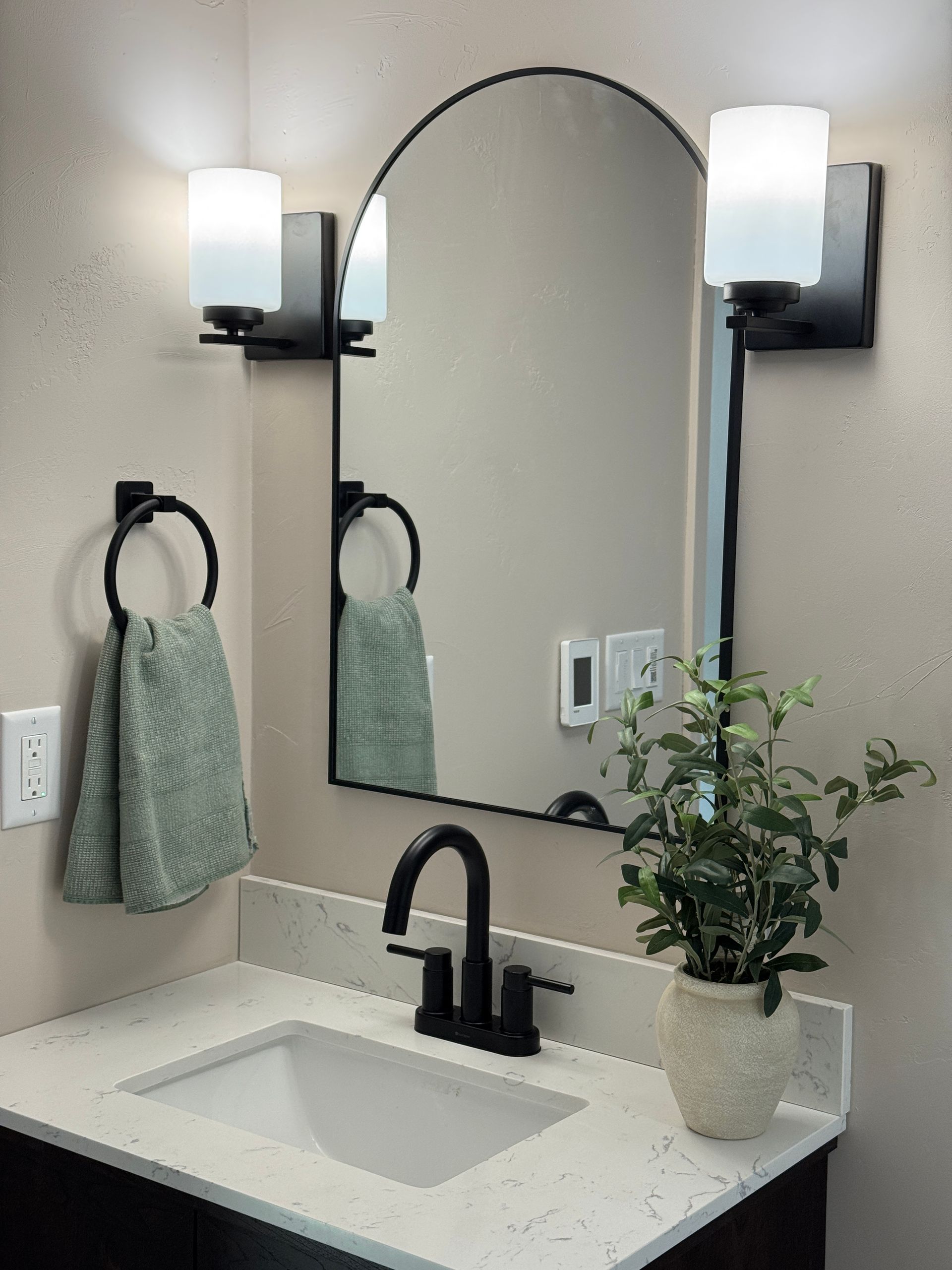 Bathroom vanity with black fixtures, white countertop, arched mirror, and green towel.