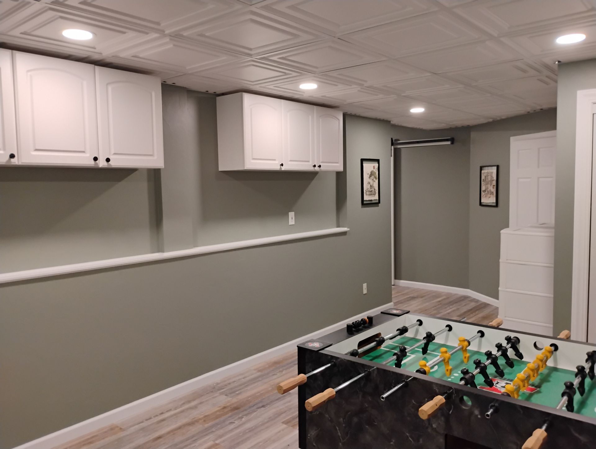 A finished basement with a foosball table, cabinets, and a low wall
