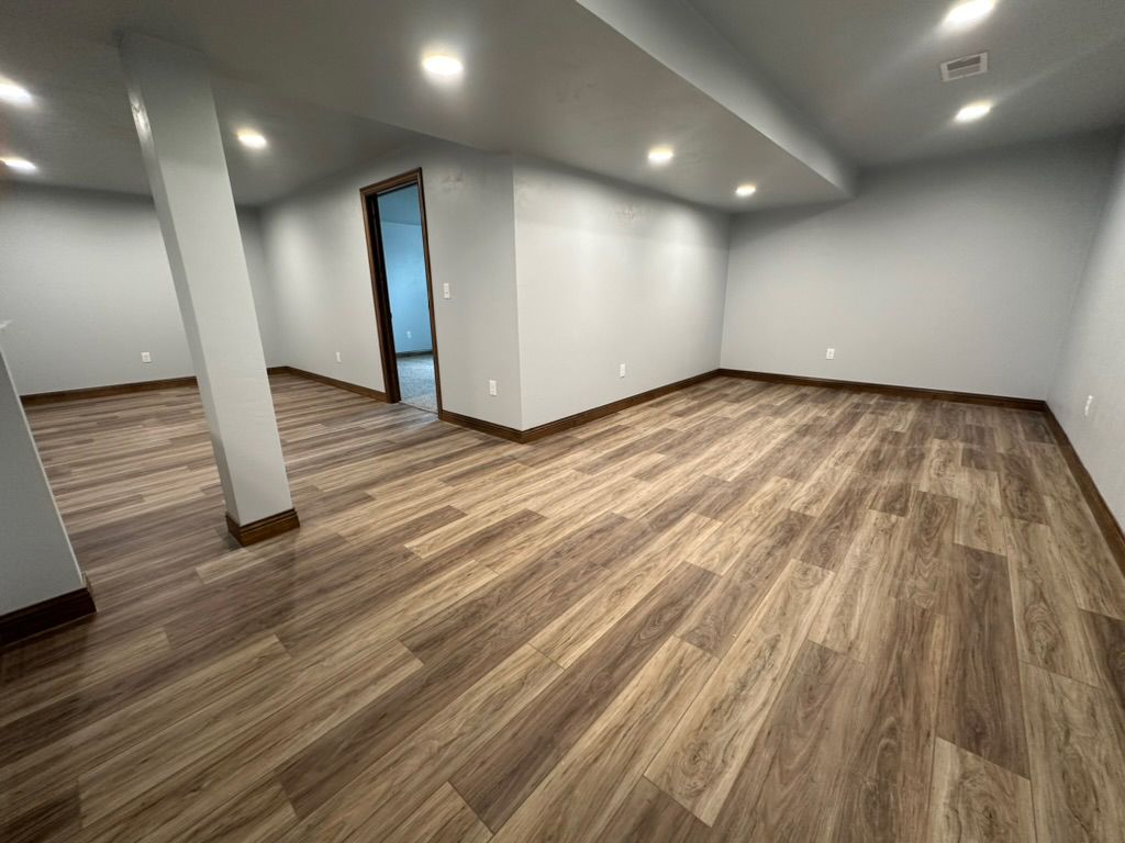 An empty basement with hardwood floors and white walls.