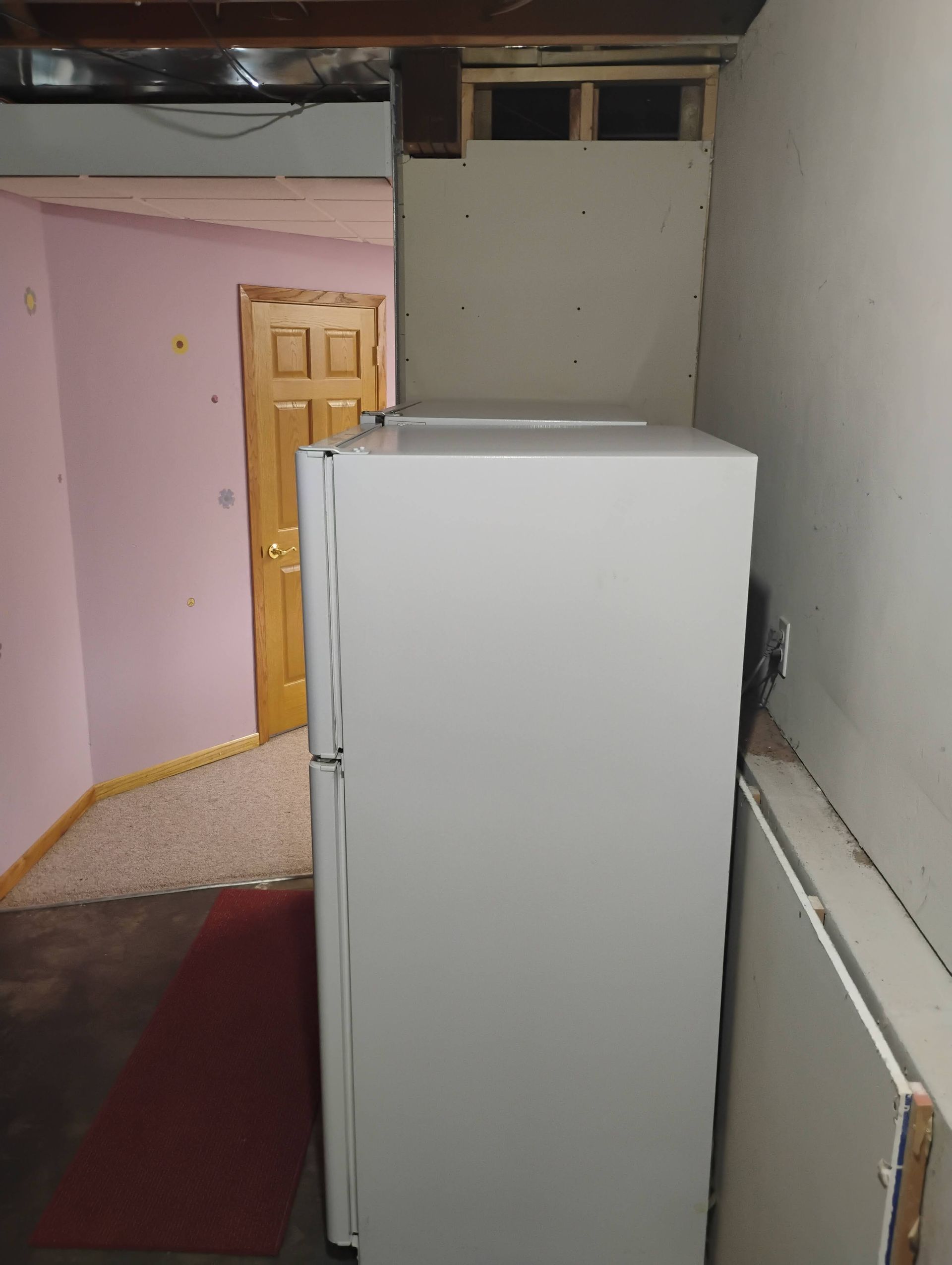 White refrigerator in a narrow basement hallway, blocking some of the doorway