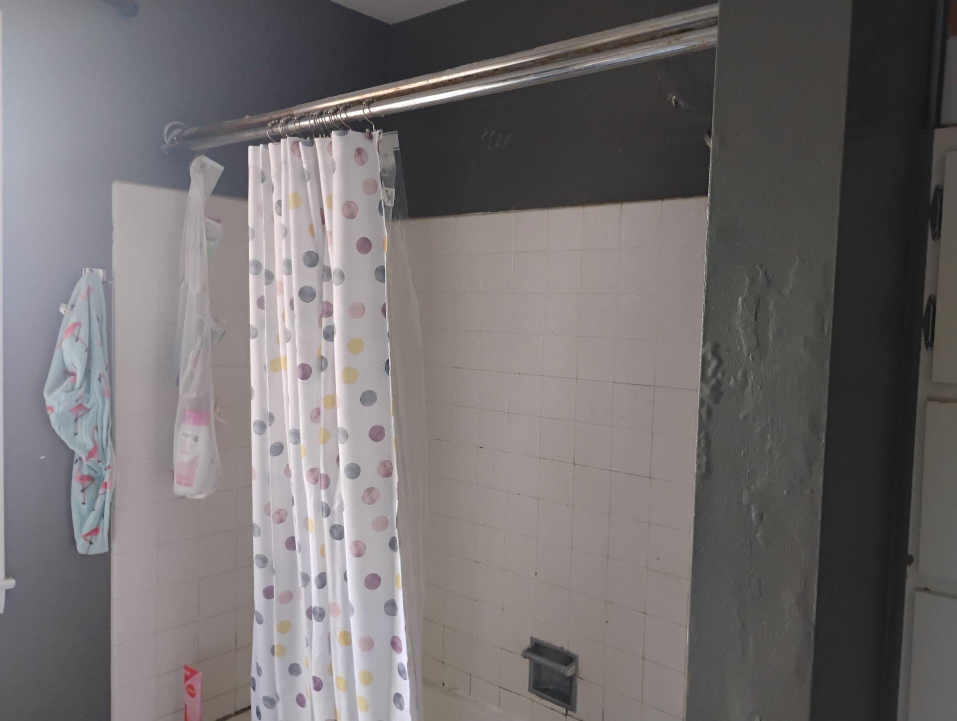Bathroom with a white shower, curtain with colorful polka dots, dark gray wall and a gray support beam