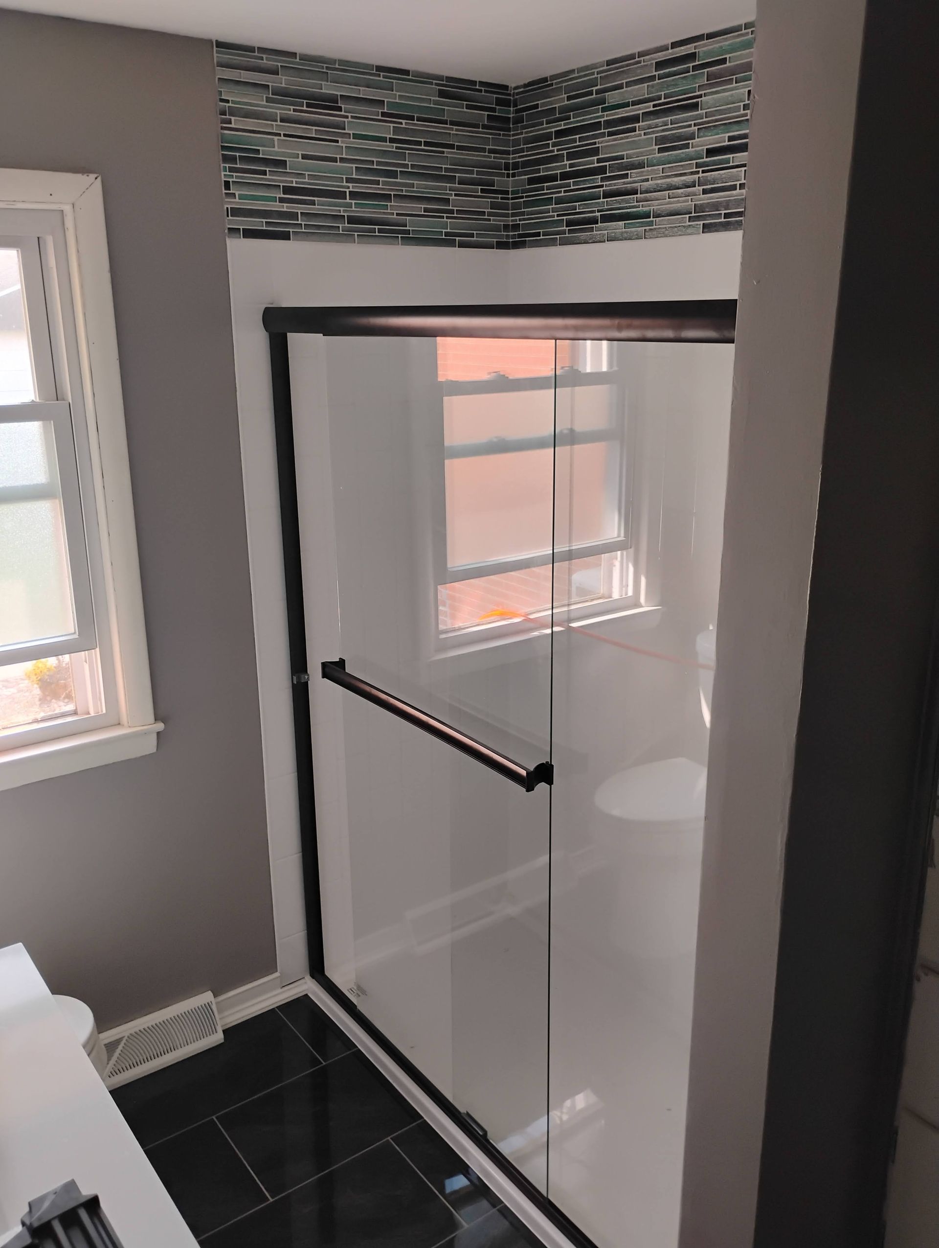 Bathroom with a black-framed shower door, white interior, and mosaic tile accent above