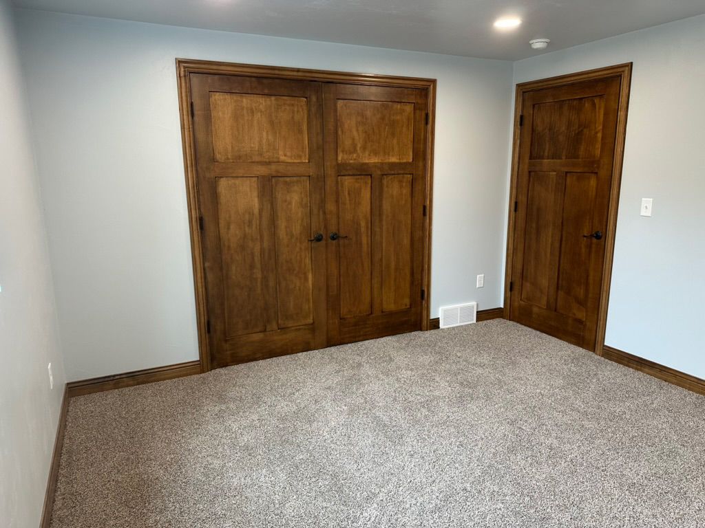 An empty room with two wooden doors and a carpeted floor.
