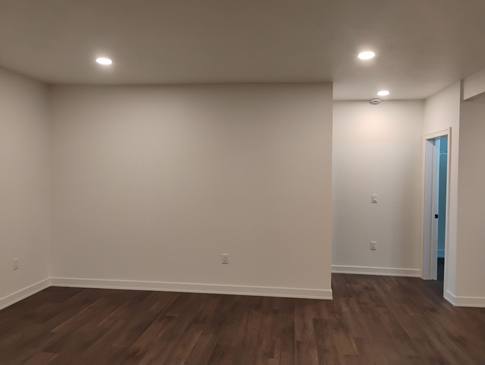 Empty room with white walls, recessed lighting, and dark wood-look flooring