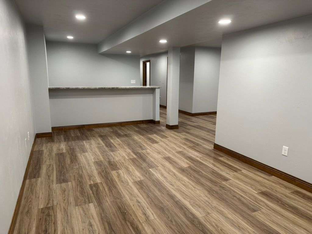 An empty basement with hardwood floors and white walls.