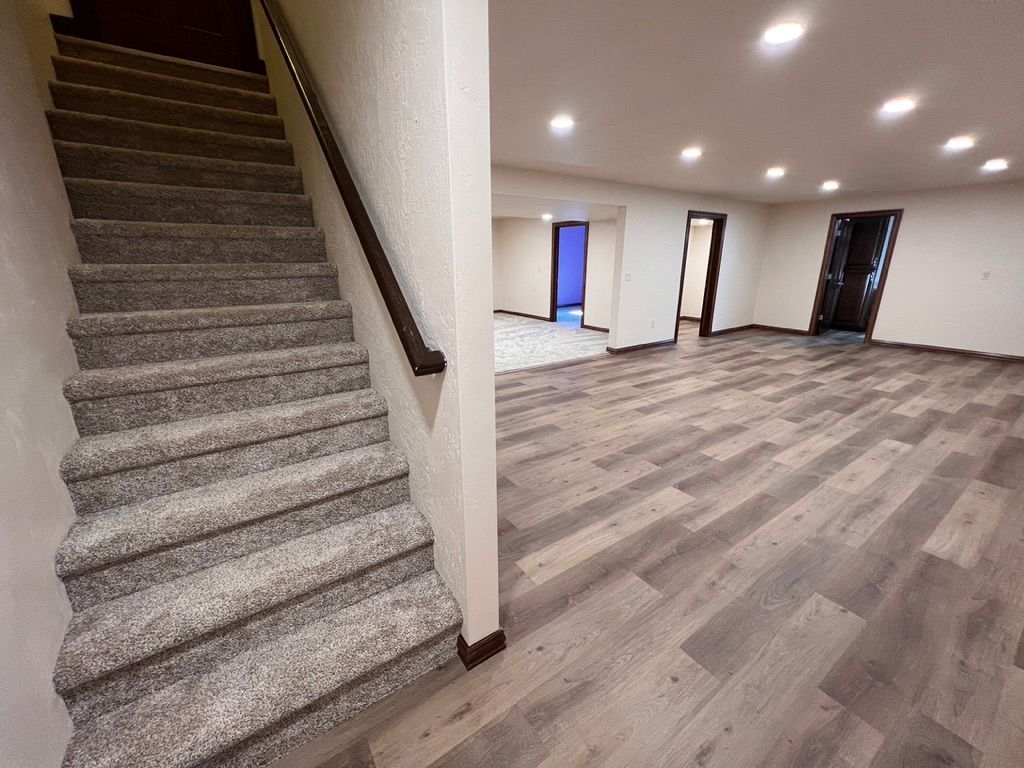 A basement with carpeted stairs and wooden floors.