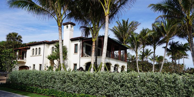 A large white house surrounded by palm trees on a sunny day.