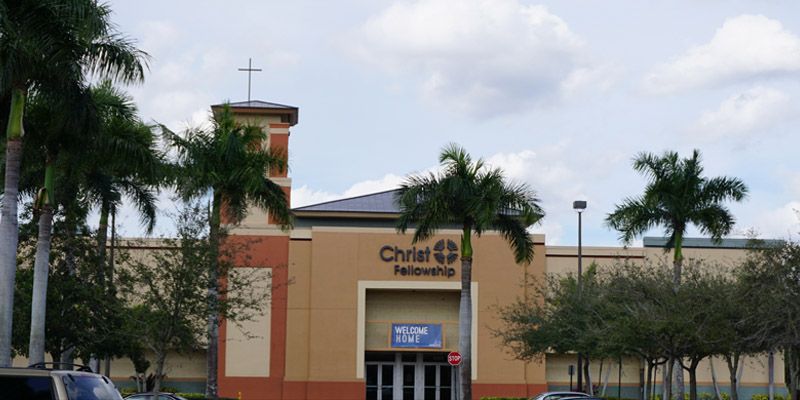 A church with a cross on top of it is surrounded by palm trees.