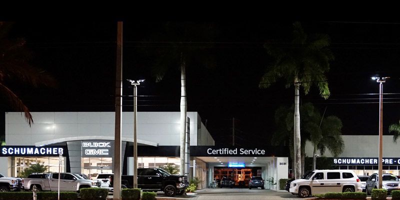 A gmc dealership is lit up at night with cars parked in front of it.