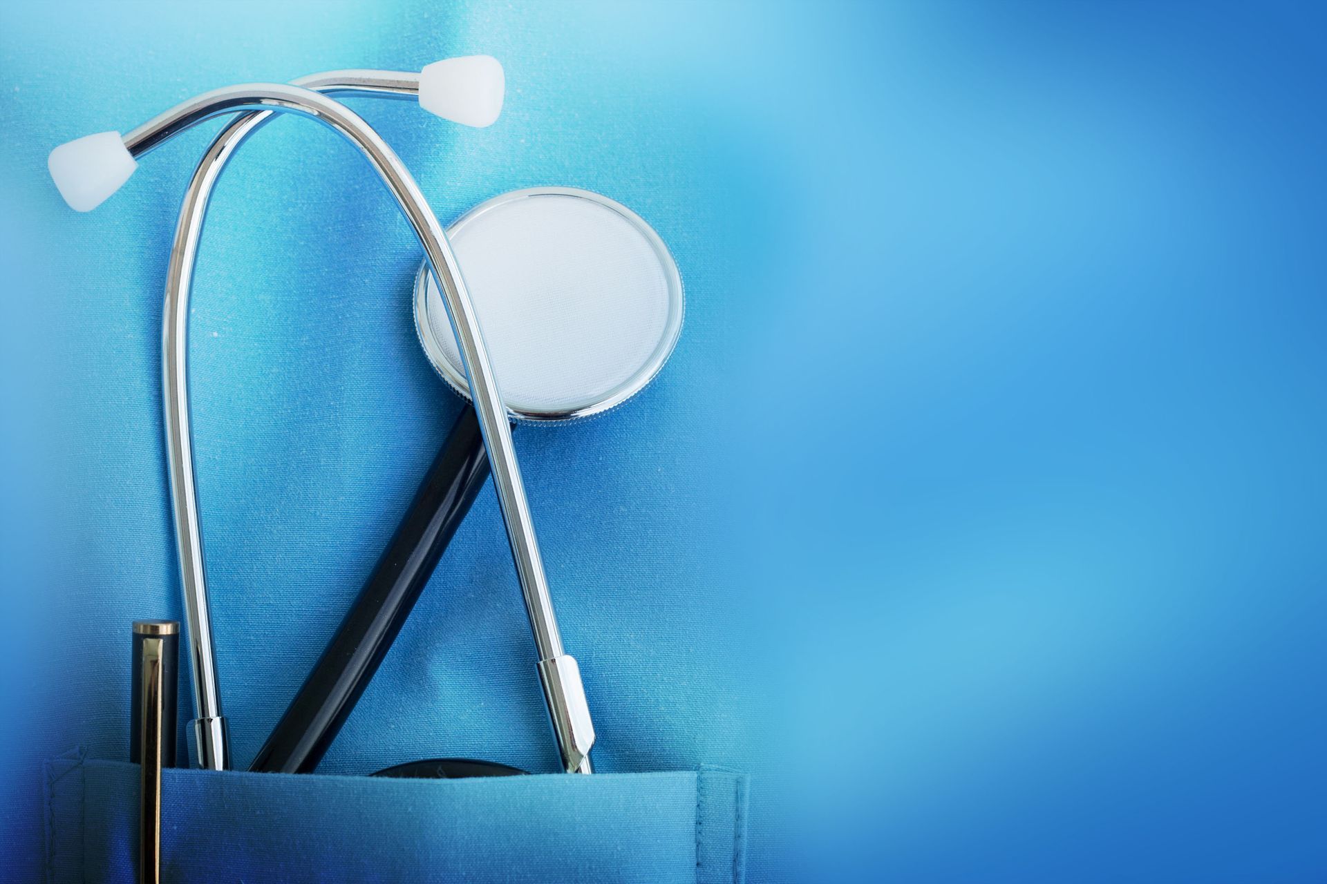 Stethoscope and pen in the pocket of a blue medical coat against a blue background.