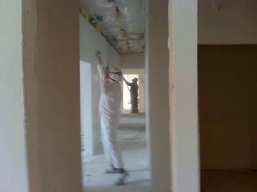 A man is standing in a hallway painting a wall.