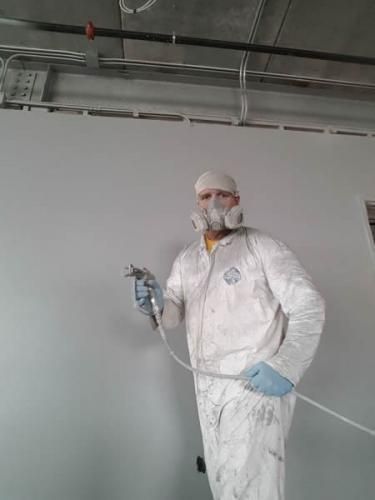 A man in a protective suit is spray painting a wall.