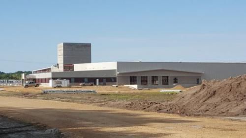 A large building is being built in a field with a pile of dirt in front of it.